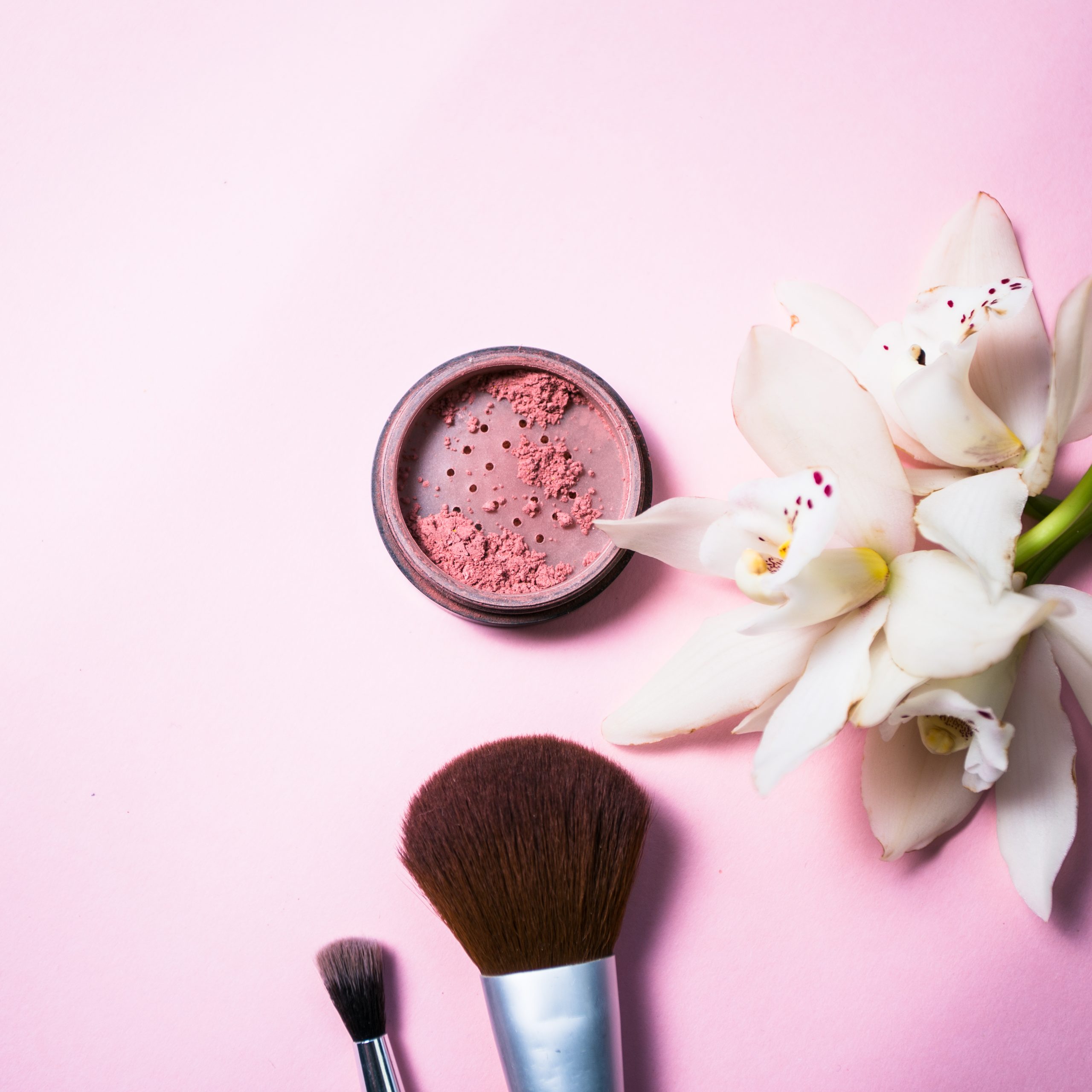 Powder, brush and flower on pink background